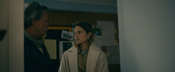 Movie still from “Acidman” (2022), directed by Alex Lehmann – A woman wearing a white coat standing next to a wall; Medium shot, Over the shoulder angle