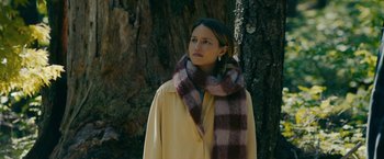 Movie still from “Acidman” (2022), directed by Alex Lehmann – A woman wearing a coat and a scarf standing in front of a tree; Medium shot, Low angle
