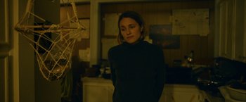 Movie still from “Acidman” (2022), directed by Alex Lehmann – A woman standing in front of a tree in a dark room; Medium shot, Over the shoulder angle