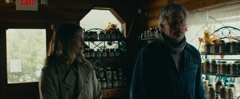 Movie still from “Acidman” (2022), directed by Alex Lehmann – A man and a woman standing next to each other in front of shelves filled with jars; Medium shot, Over the shoulder angle