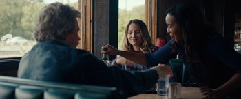 Movie still from “Acidman” (2022), directed by Alex Lehmann – Three people sitting at a table with drinks; Medium shot, Over the shoulder angle
