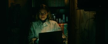 Movie still from “Acidman” (2022), directed by Alex Lehmann – A woman sitting in front of a laptop computer; Medium shot, Low angle