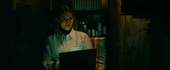 Movie still from “Acidman” (2022), directed by Alex Lehmann – A woman sitting in front of a laptop computer; Medium shot, Low angle