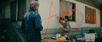 Movie still from “Acidman” (2022), directed by Alex Lehmann – Two people are painting a wall with orange paint; Medium shot, Over the shoulder angle