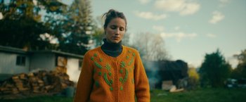 Movie still from “Acidman” (2022), directed by Alex Lehmann – A woman in a sweater standing in the grass; Medium shot, Low angle