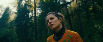 Movie still from “Acidman” (2022), directed by Alex Lehmann – A woman wearing a sweater standing in the woods; Close Up shot, Low angle