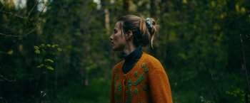 Movie still from “Acidman” (2022), directed by Alex Lehmann – A woman wearing a sweater standing in the woods; Close Up shot, Low angle