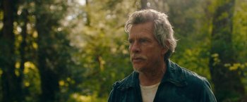 Movie still from “Acidman” (2022), directed by Alex Lehmann – An older man with a gray beard is standing in the woods; Close Up shot, Over the shoulder angle