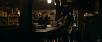 Movie still from “Acidman” (2022), directed by Alex Lehmann – Two women are standing at a counter in a store; Medium shot, Low angle