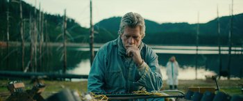 Movie still from “Acidman” (2022), directed by Alex Lehmann – An older man sitting in front of a body of water; Medium shot, Over the shoulder angle