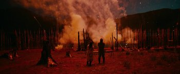 Movie still from “Acidman” (2022), directed by Alex Lehmann – Two people standing in front of a forest fire at night; Extreme Wide shot, Over the shoulder angle