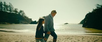 Movie still from “Acidman” (2022), directed by Alex Lehmann – An older man and a young girl walking on the beach; Wide shot, Low angle
