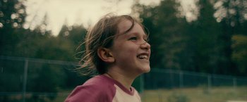Movie still from “Acidman” (2022), directed by Alex Lehmann – A little girl smiling and looking to the side; Close Up shot, Over the shoulder angle