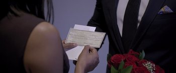 Movie still from “Acrimony” (2018), directed by Tyler Perry – A person holding a check in front of a man holding a rose; Extreme Close Up shot, Over the shoulder angle