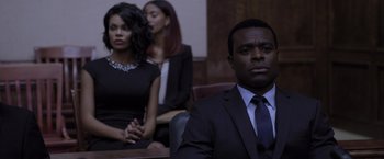 Movie still from “Acrimony” (2018), directed by Tyler Perry – A man in a black suit sitting in front of two other people; Medium shot, Over the shoulder angle