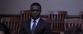 Movie still from “Acrimony” (2018), directed by Tyler Perry – A man wearing a suit and tie sitting in a courtroom; Medium shot, Over the shoulder angle
