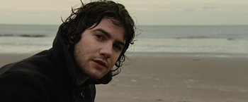 Movie still from “Across the Universe” (2007), directed by Julie Taymor – A person on a beach near the ocean; Close Up shot, Over the shoulder angle