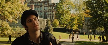 Movie still from “Across the Universe” (2007), directed by Julie Taymor – A young man in a black hat is standing in front of a building; Close Up shot, Over the shoulder angle