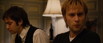 Movie still from “Across the Universe” (2007), directed by Julie Taymor – A man with long blonde hair standing next to another man with blonde hair; Close Up shot, Over the shoulder angle