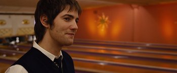 Movie still from “Across the Universe” (2007), directed by Julie Taymor – A man in a suit and tie in front of an orange wall; Close Up shot, Over the shoulder angle