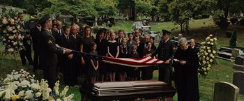 Movie still from “Across the Universe” (2007), directed by Julie Taymor – A group of people standing next to an american flag on top of a casket in a cemetary; Wide shot, High angle