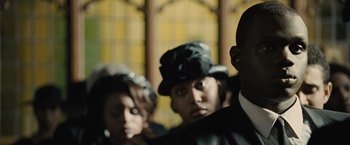 Movie still from “Across the Universe” (2007), directed by Julie Taymor – A group of people standing next to each other in a room; Close Up shot, Over the shoulder angle