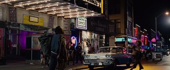 Movie still from “Across the Universe” (2007), directed by Julie Taymor – People walking on the sidewalk in front of a theater; Wide shot, High angle