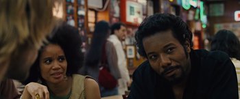 Movie still from “Across the Universe” (2007), directed by Julie Taymor – A man sitting in front of other people in a room; Close Up shot, Over the shoulder angle