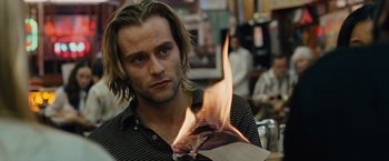 Movie still from “Across the Universe” (2007), directed by Julie Taymor – A man is holding a paper on fire; Close Up shot, Over the shoulder angle