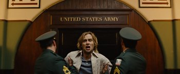 Movie still from “Across the Universe” (2007), directed by Julie Taymor – A man is being held up by two military men; Medium shot, Low angle