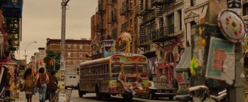 Movie still from “Across the Universe” (2007), directed by Julie Taymor – A colorful bus driving down a street with people sitting on top of it; Wide shot, Low angle