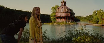 Movie still from “Across the Universe” (2007), directed by Julie Taymor – A woman standing in front of a house near a body of water; Wide shot, Low angle