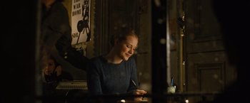 Movie still from “Across the Universe” (2007), directed by Julie Taymor – A woman sitting at a table writing on a piece of paper; Medium shot, Over the shoulder angle