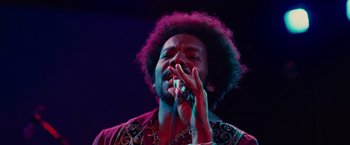 Movie still from “Across the Universe” (2007), directed by Julie Taymor – A man with a curly hair and a beard is holding a microphone; Close Up shot, Low angle