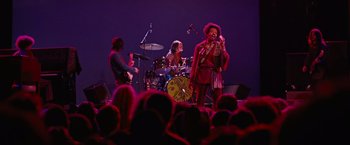 Movie still from “Across the Universe” (2007), directed by Julie Taymor – A group of people on a stage with a microphone; Wide shot, Low angle