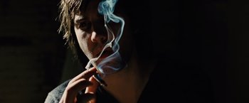 Movie still from “Across the Universe” (2007), directed by Julie Taymor – A man is smoking a cigarette in the dark; Close Up shot, Low angle