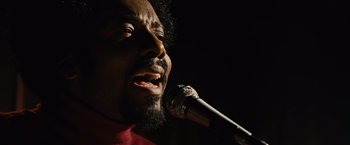 Movie still from “Across the Universe” (2007), directed by Julie Taymor – A person holding a microphone; Close Up shot, Low angle