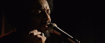 Movie still from “Across the Universe” (2007), directed by Julie Taymor – A person singing on a microphone; Close Up shot, Low angle