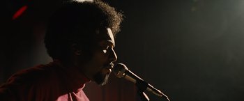 Movie still from “Across the Universe” (2007), directed by Julie Taymor – A man with a beard is singing into a microphone; Close Up shot, Low angle
