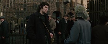 Movie still from “Across the Universe” (2007), directed by Julie Taymor – A group of men in hats and coats standing next to each other on a sidewalk; Medium shot, Over the shoulder angle