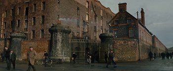 Movie still from “Across the Universe” (2007), directed by Julie Taymor – A group of people walking in front of an old brick building; Extreme Wide shot, High angle