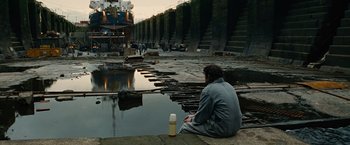 Movie still from “Across the Universe” (2007), directed by Julie Taymor – A man sitting next to a body of water; Wide shot, High angle