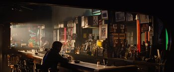 Movie still from “Across the Universe” (2007), directed by Julie Taymor – A man sitting at a bar with a cup in his hand; Wide shot, Over the shoulder angle