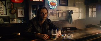 Movie still from “Across the Universe” (2007), directed by Julie Taymor – A man sitting at a table with a glass of beer; Medium shot, Over the shoulder angle