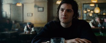 Movie still from “Across the Universe” (2007), directed by Julie Taymor – A man sitting at a table with a glass in front of him; Close Up shot, Over the shoulder angle