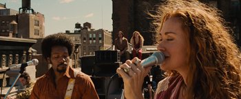 Movie still from “Across the Universe” (2007), directed by Julie Taymor – A group of people standing on top of a building with a microphone; Medium shot, Low angle
