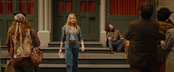 Movie still from “Across the Universe” (2007), directed by Julie Taymor – A woman standing on the steps of a building next to a man sitting on the steps; Wide shot, Low angle