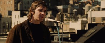 Movie still from “Across the Universe” (2007), directed by Julie Taymor – A man with long brown hair standing in front of a microphone; Close Up shot, Over the shoulder angle