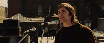 Movie still from “Across the Universe” (2007), directed by Julie Taymor – A man standing in front of two microphones; Close Up shot, Over the shoulder angle