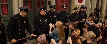 Movie still from “Across the Universe” (2007), directed by Julie Taymor – A group of men and women standing around a woman; Medium shot, Over the shoulder angle